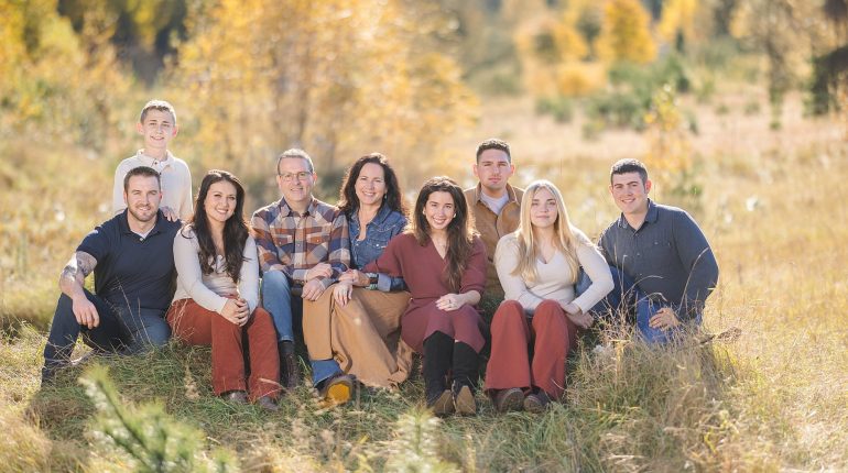 A multi-generational family sitting naturally on a grassy slope in a Vermont meadow during the fall, photographed by a professional Vermont family lifestyle photographer. The image highlights the natural interactions and timeless visual legacy typical of lifestyle photography sessions.