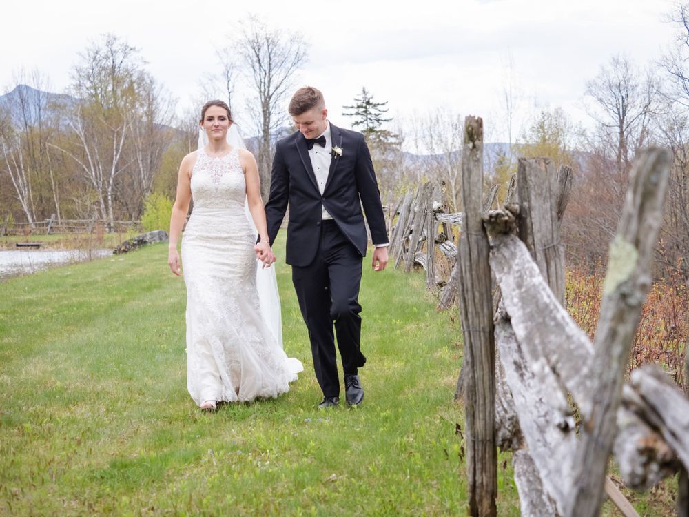 A bride and groom walking along a rustic fence in a Vermont meadow, captured by an affordable wedding photographer VT