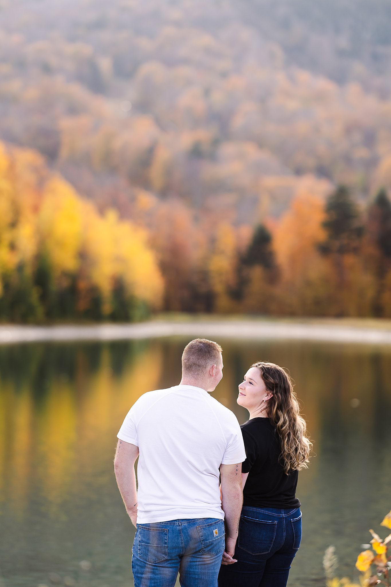 A couple looking at each other by a lake during a session with a professional photographer Vermont.