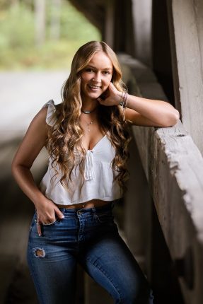 A smiling high school senior girl posing inside a rustic covered bridge in Vermont.