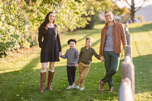 A family of four holding hands along a rustic fence during a session with a Vermont family photographer.