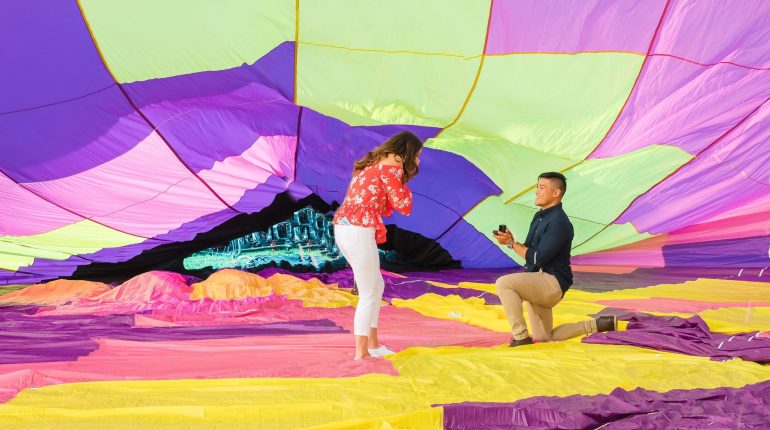 A man proposes on one knee inside a colorful balloon during a Vermont engagement photography session.
